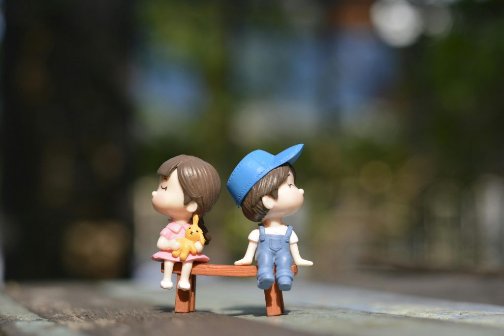 Adorable figurines of a boy and girl sit on a bench, bathed in summer sunlight.